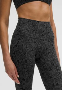 Aukštos juosmens tamprės tamsiai pilkos spalvos audiniu su subtiliu gėlių raštu. Medžiaga atrodo elastinga ir turi lygų paviršių.