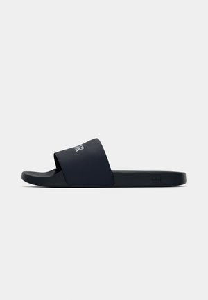 Black slide sandal with wide textured strap and white logo text, flat sole, and slight arch support, shown from side on white background.