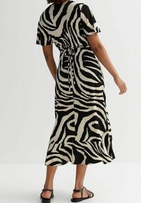 Musta-beige raidallinen mekkö, jossa lyhyet hihat, rento istuvuus ja vyötäröltä kiristetty, valmistettu kevyestä kankaasta.