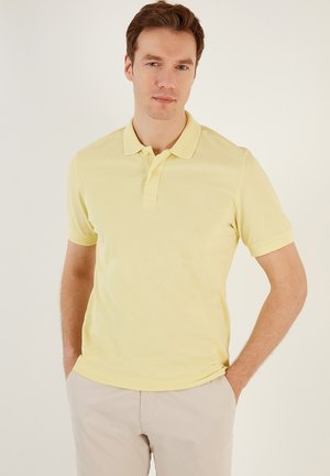 Polo giallo in un morbido materiale a maglia, con colletto classico, pattina con tre bottoni e maniche corte con polsini testurizzati.