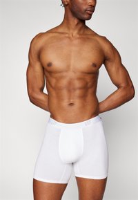Boxers en coton blanc avec une coupe slim, dotés d'une ceinture douce embossée avec "GAP". Texture lisse et sans motifs visibles.