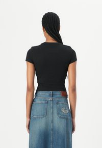Černý krátký rukávový crop top s kulatým výstřihem, částečně kombinovaný s modrou džínsovou sukní s vyšívanými detaily a koženou nášivkou na pásku.
