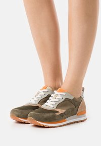 Låga sneakers i olivgrön och beige mocka, med meshpaneler, orange detaljer och vita snören. Texturerad gummisula synlig.
