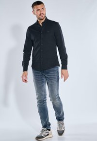 Dunkelblaues Baumwollhemd mit Knopfleiste, taillierte Passform mit langen Ärmeln, getragen mit hellblauen Jeans und grauen Sneakers.