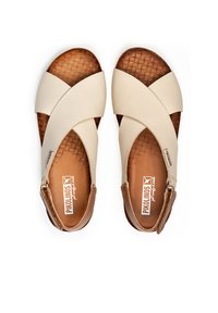 Beżowe skórzane sandały z krzyżującymi się paskami, plecioną teksturą na podeszwie i brązowymi akcentami. Regulowany pasek zapewniający pewne dopasowanie.