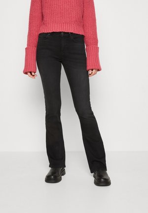 Person iført sorte bootcut-jeans, sorte chunky støvler og en pink chunky striktrøje med forlængede manchetter.