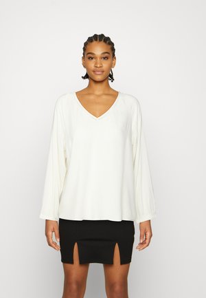 Blusa branca de manga longa com decote em V e gola costurada, combinada com uma saia mini preta com duas fendas frontais. Textura suave.