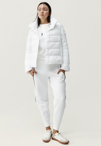 Chaqueta de plumas blanca con diseño recortado y patrón de acolchado horizontal, combinada con pantalones de chándal a juego que tienen rayas laterales y puños elásticos.
