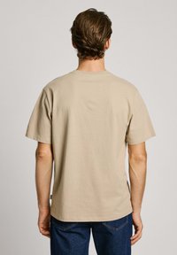 Beige cotton T-shirt with a crew neck and short sleeves, featuring a relaxed fit and plain back design, paired with dark jeans.