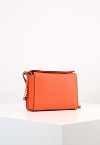 Orange läderhandväska med rektangulär form, slät yta och en kedjestrappram. Har en dragkedjestängning på toppen.