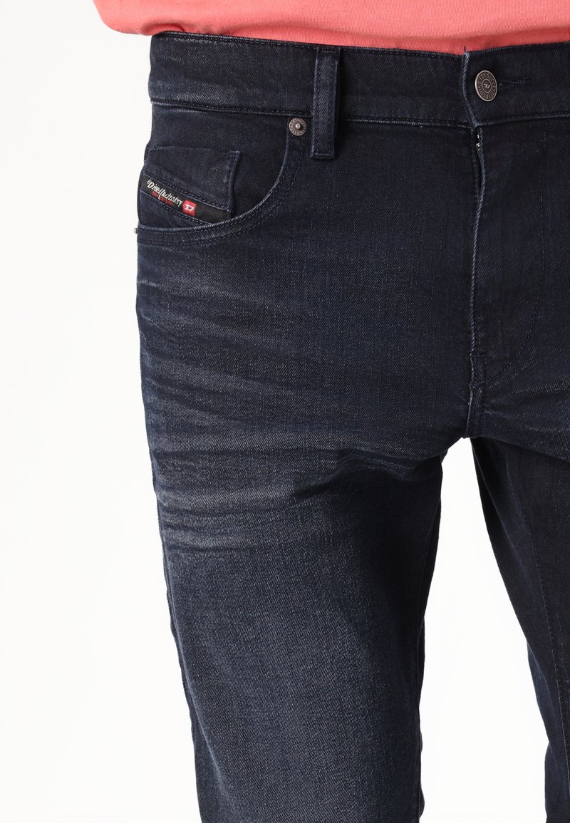 Jean en denim bleu foncé avec un léger délavage, design à cinq poches et étiquette de marque sur la poche avant, dotés de quincaillerie en ton argent.