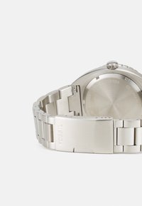 Orologio in acciaio inox argento con finitura spazzolata. Presenta un bracciale solido, una cassa rotonda e una fibbia incisa prominente con la scritta "FOSSIL."