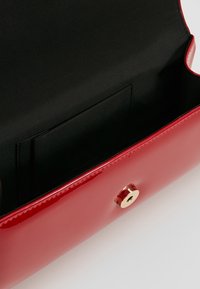 Borsa a mano in pelle patinata rossa con finitura lucida, tasca interna e chiusura in metallo dorato. La fodera in tessuto nera crea contrasto.