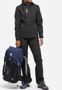 Veste softshell noire avec col haut, pantalon ajusté et un sac à dos bleu marine et noir. Les caractéristiques clés comprennent des zips, des sangles et des matériaux texturés.