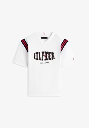 Camiseta blanca de manga corta con cuello en V, con texto "HILFIGER Since 1985", detalles de rayas en azul marino y rojo en los hombros, y pequeño logotipo en la manga izquierda.