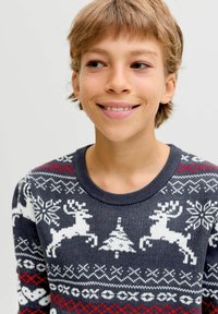 Sötétkék kötött pulóver fehér rénszarvas és hópehely mintákkal. Kerek nyakkivágással és piros díszítésekkel rendelkezik a dizájnban.