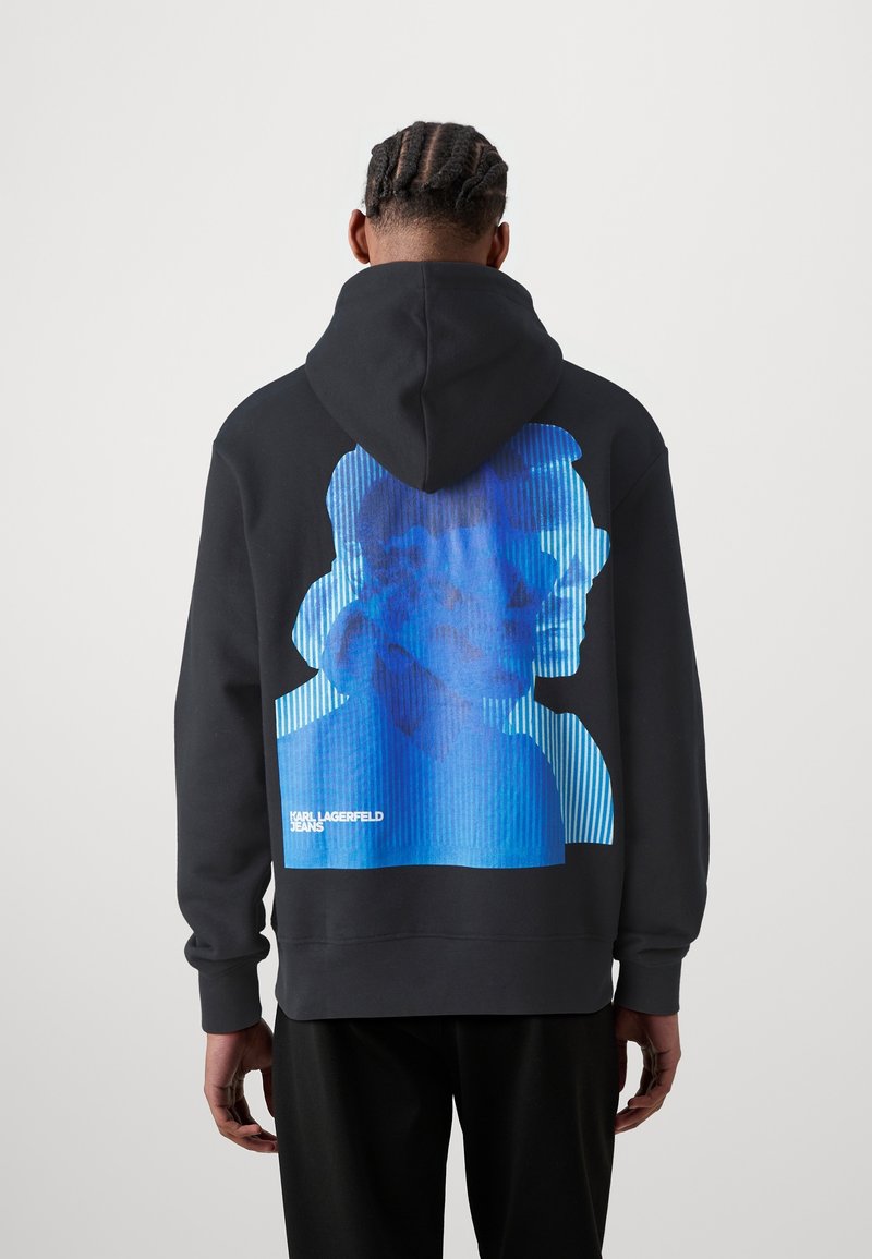 Sudadera negra con capucha y un gran diseño gráfico azul en la espalda que muestra un rostro estilizado y rayas verticales. Material de algodón.