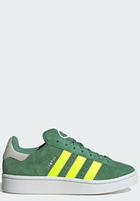 Zapatillas de ante verde con tres rayas amarillas brillantes, suela blanca y detalles de perforación. Acento de ante marrón en el talón. Diseño con cordones.