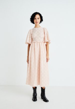 Lace midi-jurk in zachtroze met pofmouwen, diamanten patronen en een gegatherde taille. In combinatie met zwarte hoge laarzen.