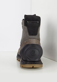 Bottine en suède gris avec tige en suède noir, semelle en caoutchouc et talon texturé. Coutures apparentes et détail du logo sur le talon arrière.