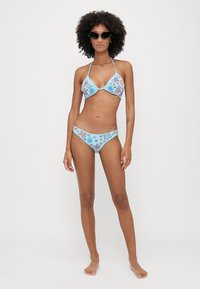 Plavi bikini set s cvjetnim uzorcima u ružičastoj i plavoj boji, s trokutastim vrhom i donjim dijelom niskog struka. Čini se da je materijal rastezljiv i gladak.