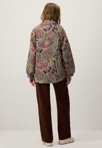 Srajca z dolgimi rokavi s potiskom paisley v večbarvnih odtenkih, z ovratnikom in sproščenim krojem, kombinirana z rjavimi širokimi hlačami.