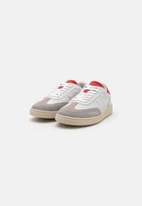 Hvite og grå semskede sneakers med røde aksenter, rund tå og teksturert gummisåle. Har hvite snørebånd og minimalistiske design detaljer.