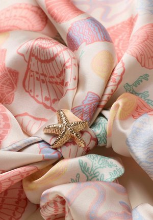 Gold textured starfish-shaped brooch on pastel fabric with pink seashell and coral prints, loosely gathered.