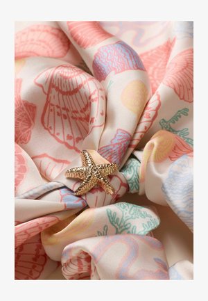 Gold textured starfish-shaped brooch on pastel fabric with pink seashell and coral prints, loosely gathered.