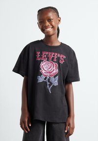 Camiseta de algodón negra con un gran gráfico de una rosa blanca y roja con el texto "LEVI'S" arriba. Corte relajado y mangas cortas, textura suave.
