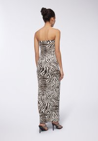Abito maxi senza spalline con stampa zebra marrone e bianca, design aderente, spacchi laterali e sandali neri con tacco alto.