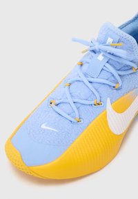Lysblå atletiksko med tekstureret stofoverdel, gul gummisål, hvid Nike swoosh og matchende blå snørebånd.