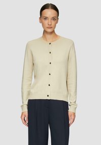 Hellbeige Strickjacke mit rundem Ausschnitt, langen Ärmeln und dunklen Knöpfen an der Vorderseite. Weiche Textur und figurbetonte Saumdetails.