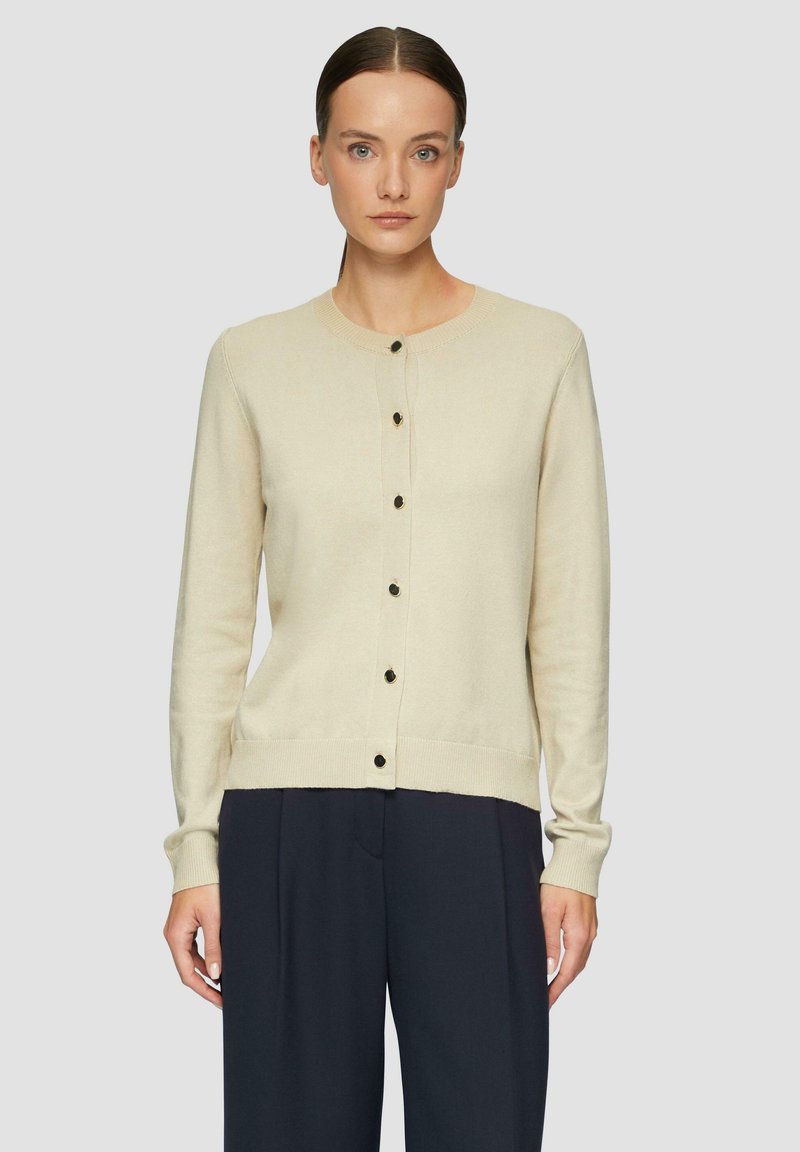 Hellbeige Strickjacke mit rundem Ausschnitt, langen Ärmeln und dunklen Knöpfen an der Vorderseite. Weiche Textur und figurbetonte Saumdetails.