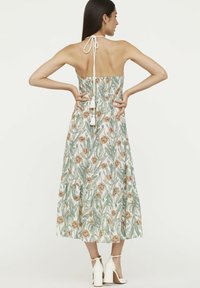 Midi-Kleid mit Blumenmuster und gerafftem Rücken, Neckholder-Bindebändern und gestuftem Rock. Die Farben umfassen weiße, grüne und braune Blumenmuster.