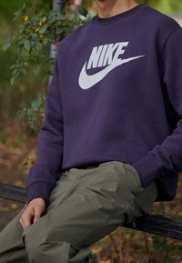 Navy-purple crewneck sweatshirt featuring a large white Nike logo, paired with olive-green cargo pants, with a smooth texture and relaxed fit.