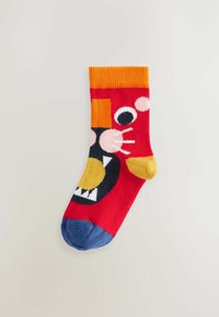 Rote Socke mit einem verspielten Cartoon-Gesicht, das orange und gelbe Akzente, eine blaue Fußspitze und ein schwarzes Mundmuster mit weißen Zähnen zeigt.