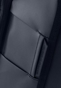 Interno in tessuto grigio scuro di una borsa con superficie strutturata. Presenta una tasca per le informazioni del proprietario e dettagli di cuciture a contrasto.