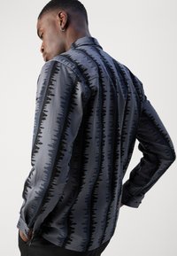Camisa de manga longa em azul marinho e cinza, apresentando um padrão de árvores contra riscas. Textura suave e gola.