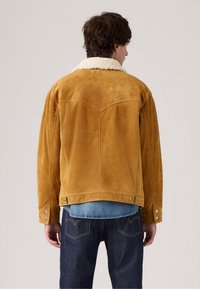 Tawny suède jas met een crèmekleurige schapenvacht kraag, featuring een western yoke ontwerp en drukknoopdetails op de manchetten. Gecombineerd met denim.