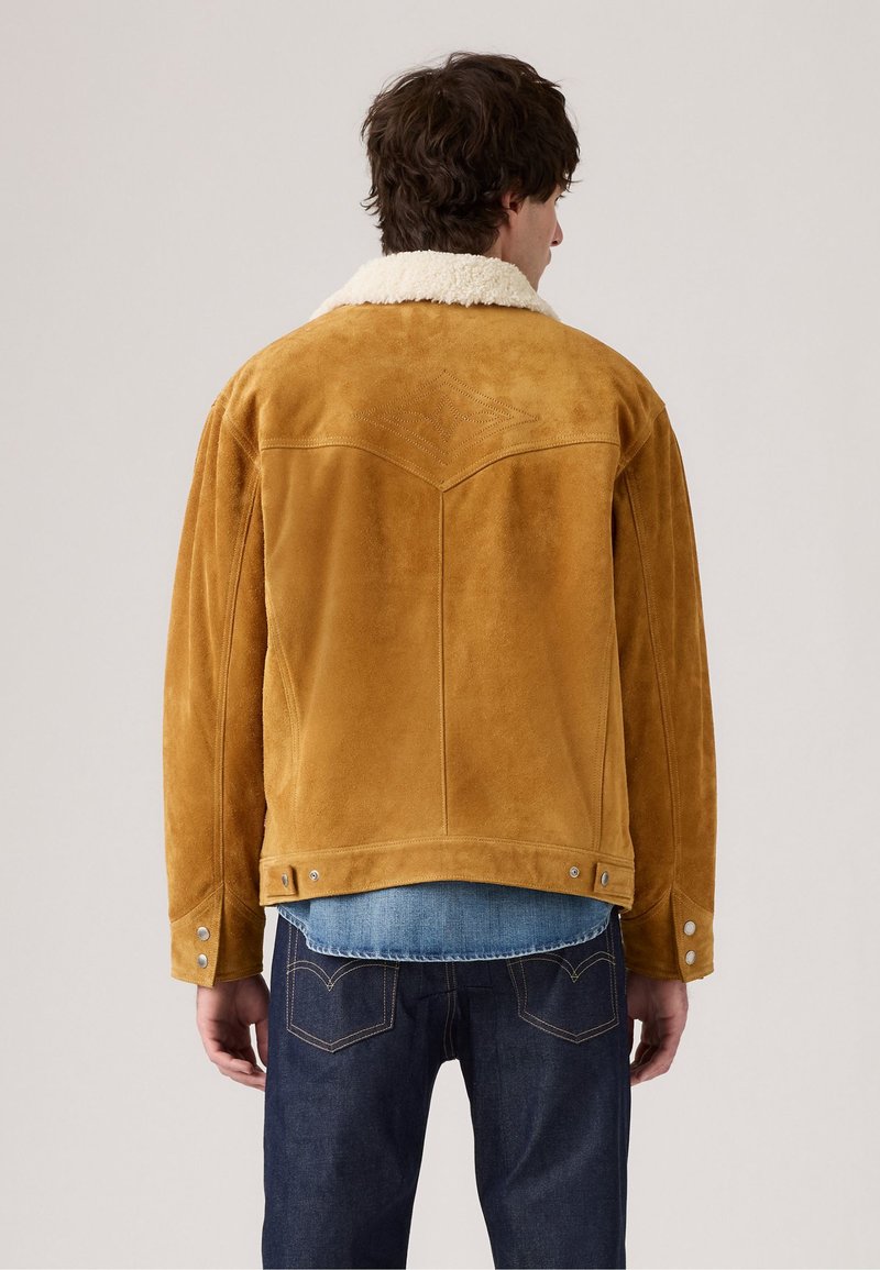 Tawny suède jas met een crèmekleurige schapenvacht kraag, featuring een western yoke ontwerp en drukknoopdetails op de manchetten. Gecombineerd met denim.