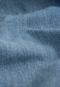 Denim szövet, világoskék színű, amelyek textúrált szövete átlós vonalakkal és finom elhalványulással rendelkezik, lágy és enyhén gyűrött megjelenést kölcsönözve.