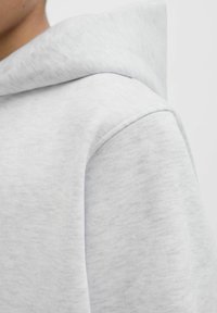 Hellgrauer Kapuzenpullover aus weichem, strukturiertem Stoff. Mit einer abgerundeten Kapuze und sichtbaren Nahtdetails an der Schulter. Minimalistisches Design.