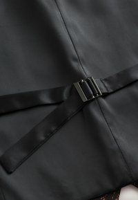 Schwarzer Stoff mit glatter Textur präsentiert einen satinierten Gürtel und eine Metallschnalle, wodurch ein maßgeschneiderter Look mit einem klaren, minimalistischen Design entsteht.