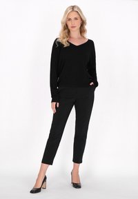 Top negru cu mânecă lungă și guler în V, asortat cu pantaloni negri slim-fit și pantofi cu toc înalt negri. Material neted cu un design confortabil.