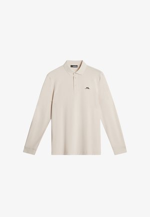 Vaaleanbeige pitkähihaine polo-paita, jossa on klassinen kaulus, kolmesta napista koostuva nappilista ja pieni musta logo vasemmassa rinnassa. Tasainen kangas.