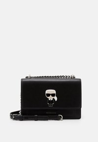 Musta nahkakäsilaukku, jossa on hopeinen ketjuhihna ja etuläpässä piirroshahmo, jolla on aurinkolasit ja puku.