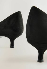 Svarta mocka högklackade skor med spetsig tå och smal klack. Texturen är mjuk och designen har en stängd bakdel.