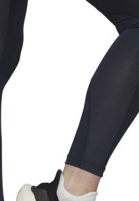 Leggings sportivi blu navy con pannello in rete testurizzata e design aderente, abbinati a una sneaker bianca e nera.