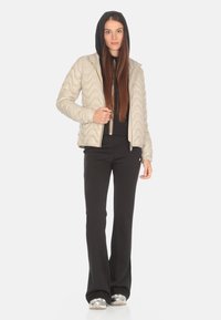 Giacca trapuntata beige chiaro con una forma aderente, cappuccio e dettagli della zip in contrasto, abbinata a pantaloni neri a zampa d'elefante e sneakers argentate.